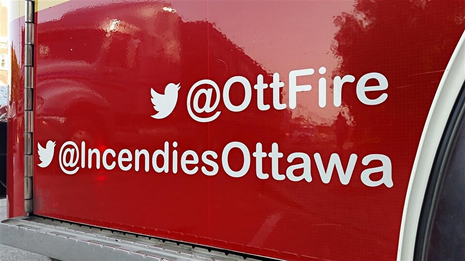Un camion de pompiers sur lequel on peut lire le nom d'utilisateur Twitter du Service des incendies d'Ottawa : « @IncendiesOttawa ».
