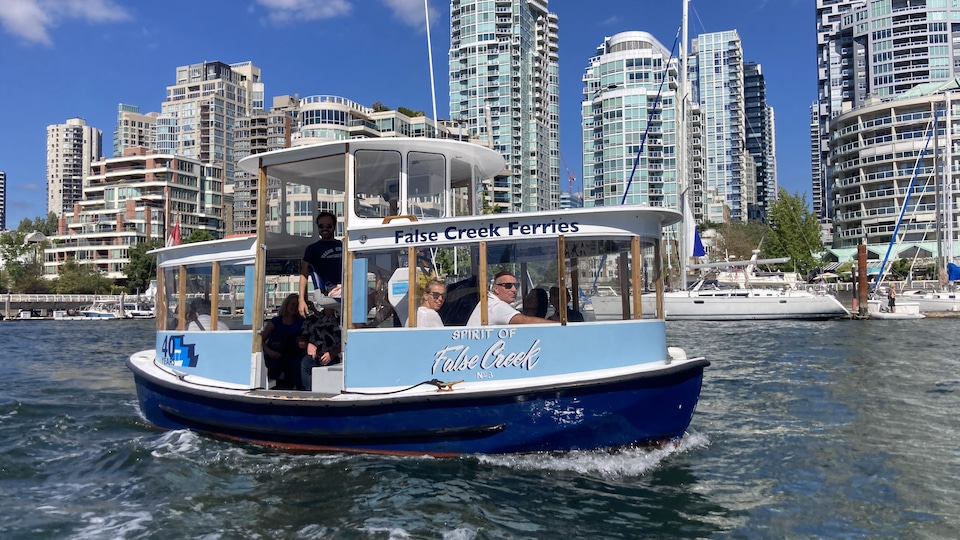 Un bateau de False Creek Ferries sur l'eau avec les immeubles de Downtown en fond.