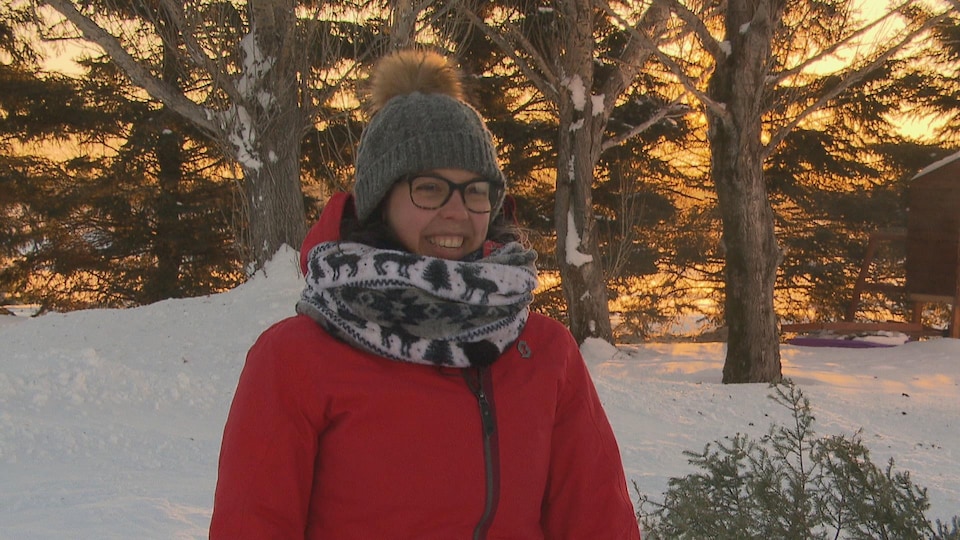 Claudia Bouchard sourit devant des arbres enneigés dans la cour de sa résidence devant le lever du soleil.