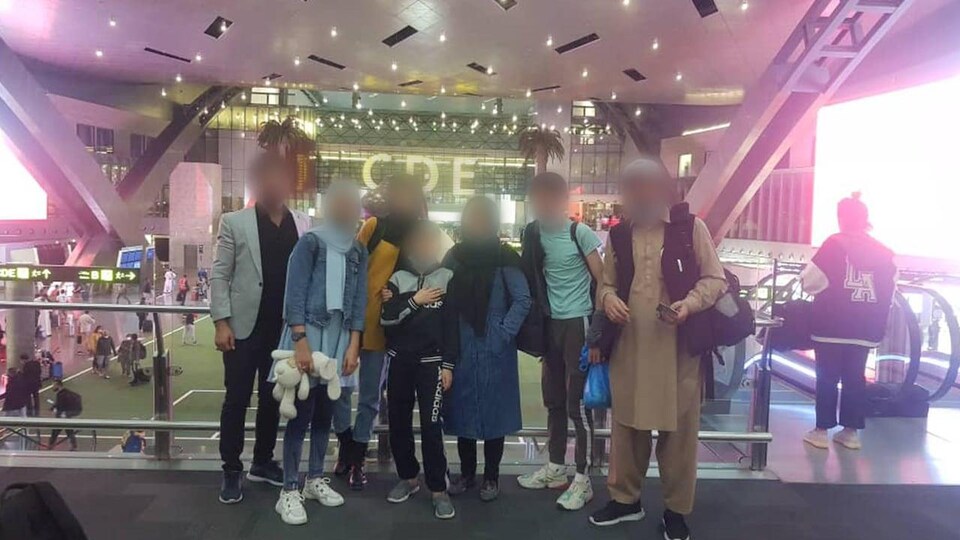 Six personnes aux visages flous (pour ne pas qu'elles soient identifiées) prennent une photo de groupe dans l'aéroport de Doha.