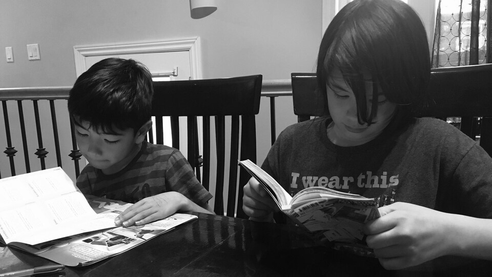 Les deux garçons sont en train de lire, assis à table.