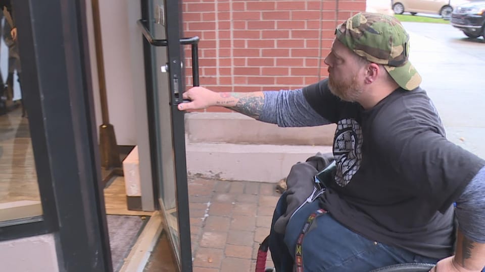 Un homme en fauteuil roulant ouvre la porte d'un commerce