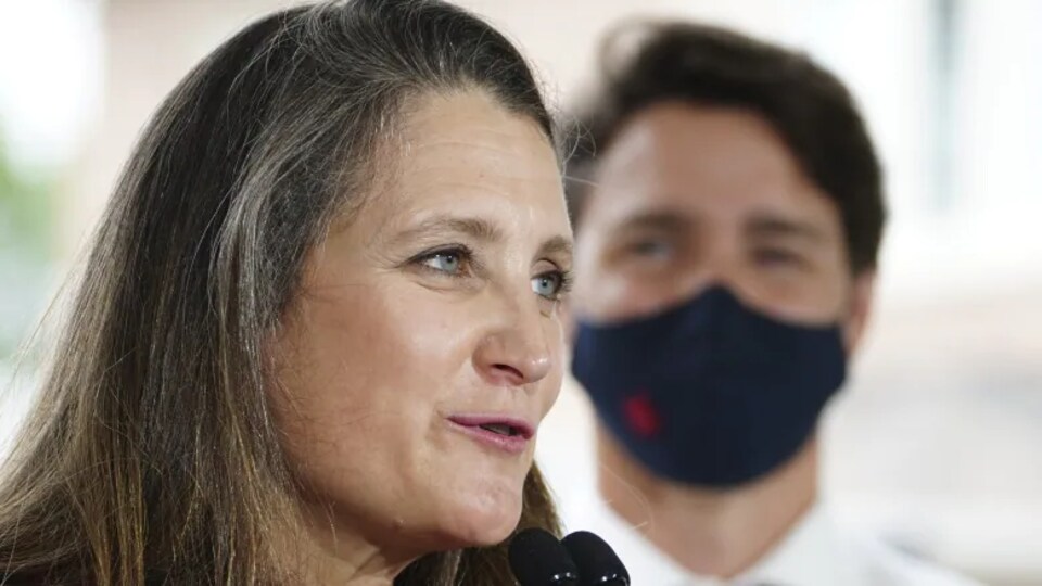 Mme Freeland parle devant un micro sous le regard de Justin Trudeau.