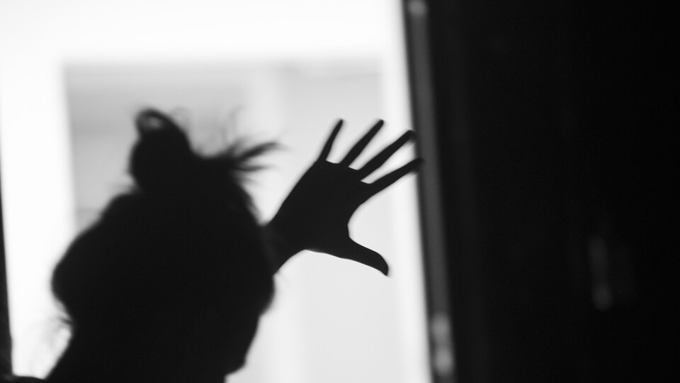 Une femme dont on ne voit que l'ombre met la main sur une fenêtre.