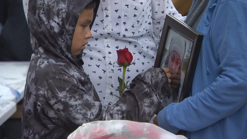 Un enfant tient une rose dans sa main et regarde tristement la photo de sa mère, Doris Trout. Une veillée a été tenue le 25 mai 2022, à Winnipeg, en sa mémoire. 