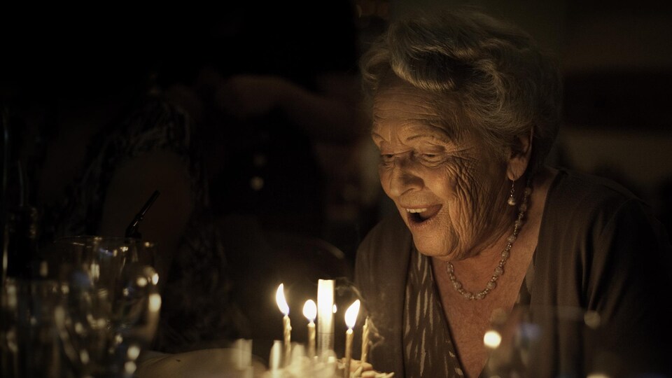 Une femme souffle les bougies de son gâteau de fête.