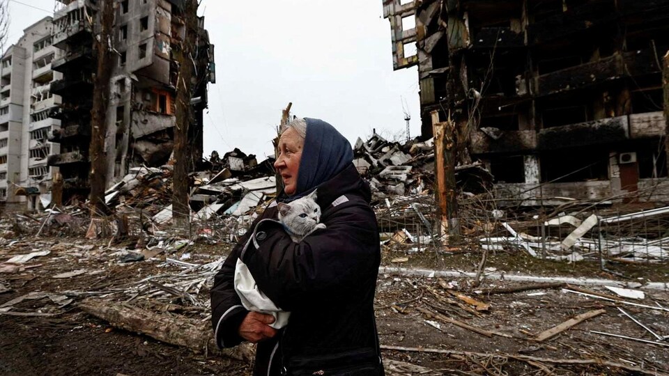 Une femme porte son chat en passant devant des bâtiments détruits par les bombardements russes.