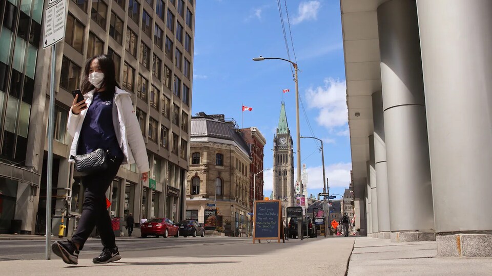 Une femme portant un masque chirurgical marche sur un trottoir du centre-ville d'Ottawa.