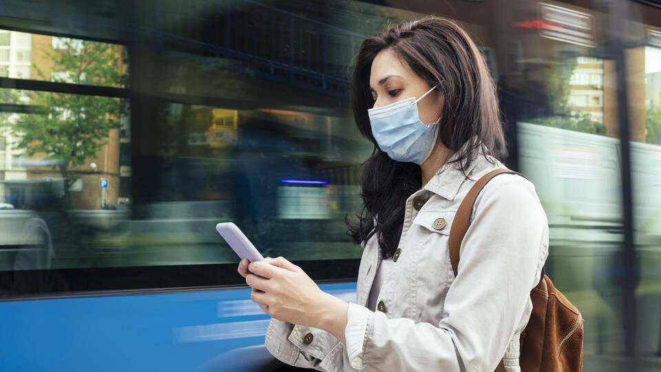 Une femme attend à un arrêt de bus. Elle porte un masque de protection pour la prévention d'un virus.