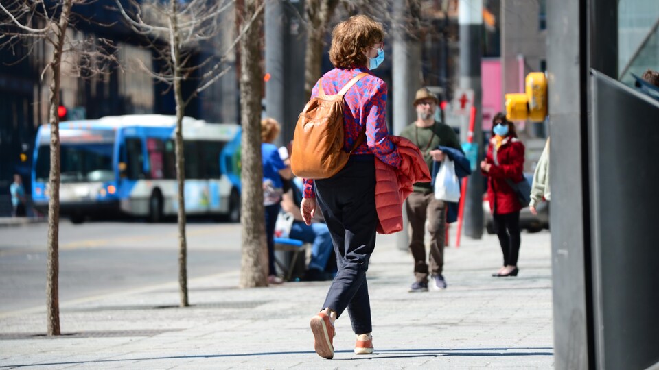 Une femme masquée marche dans une rue ensoleillée.