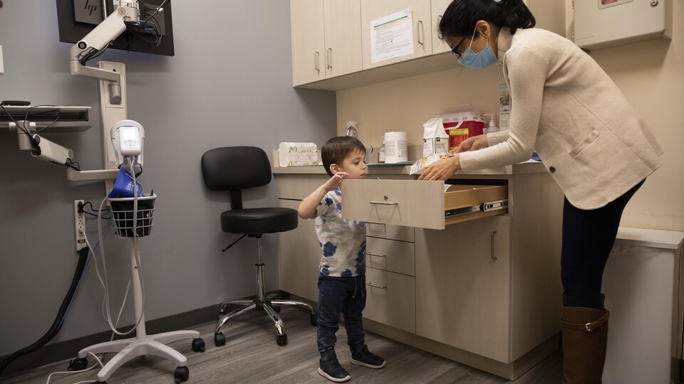 Un petit garçon examine le contenu d'un tiroir dans lequel la médecin prend quelque chose.