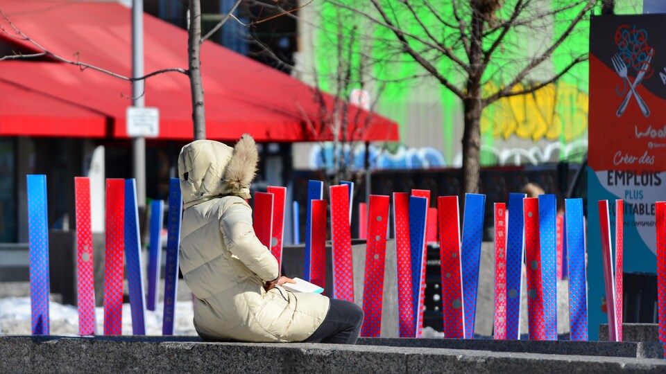 Une femme profite du soleil hivernal sur une place publique de Montréal.