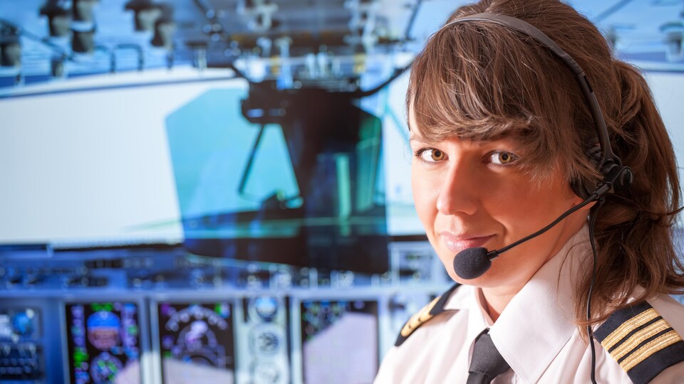 Une jeune femme dans un habit de pilote dans une cabine de pilotage.
