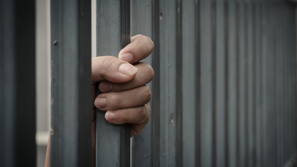 Une main de femme sur un barreau de cellule de détention.