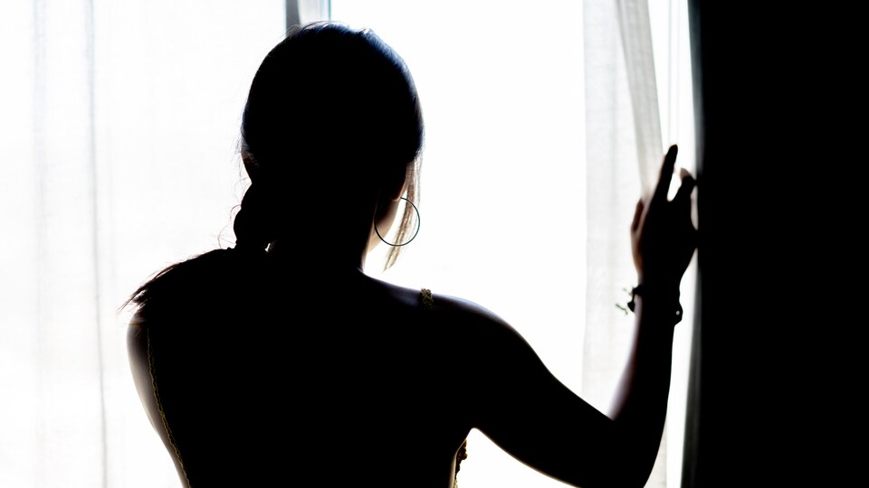 Une femme regarde au travers de rideaux et dans une fenêtre.