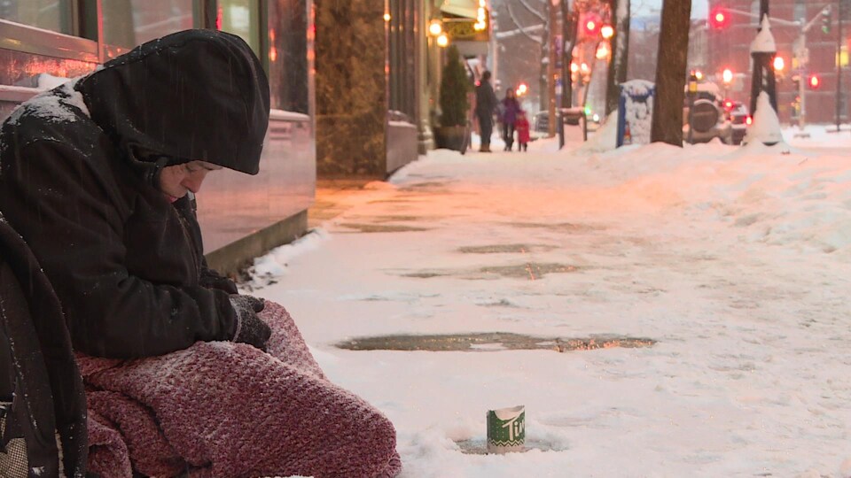 Une femme sans-abri assise sur un trottoir enneigé.