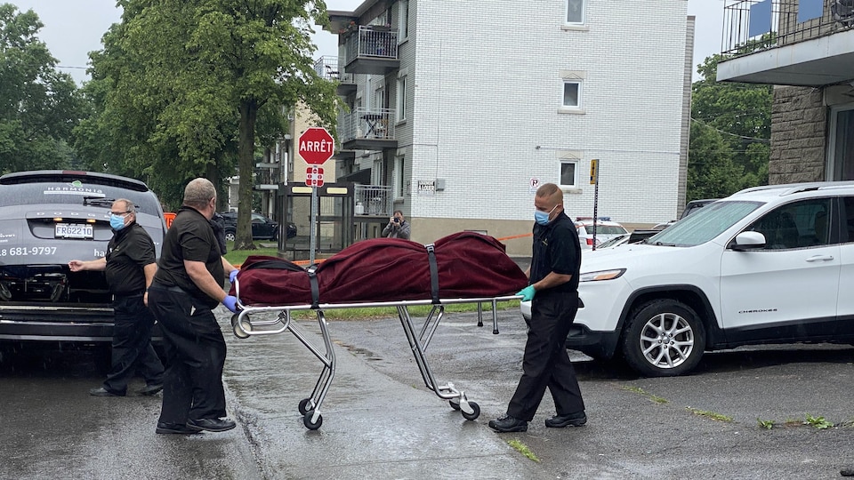 Des hommes transportent un corps enveloppé dans un drap vers une voiture appartenant à une entreprise de pompes funèbres à Québec.