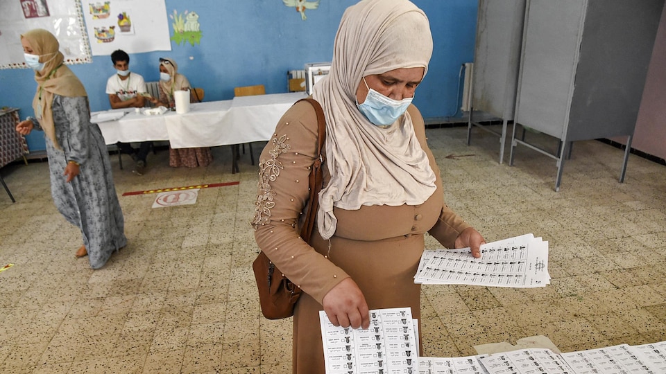 Une femme voilée et portant un masque de protection ramasse un bulletin de vote.
