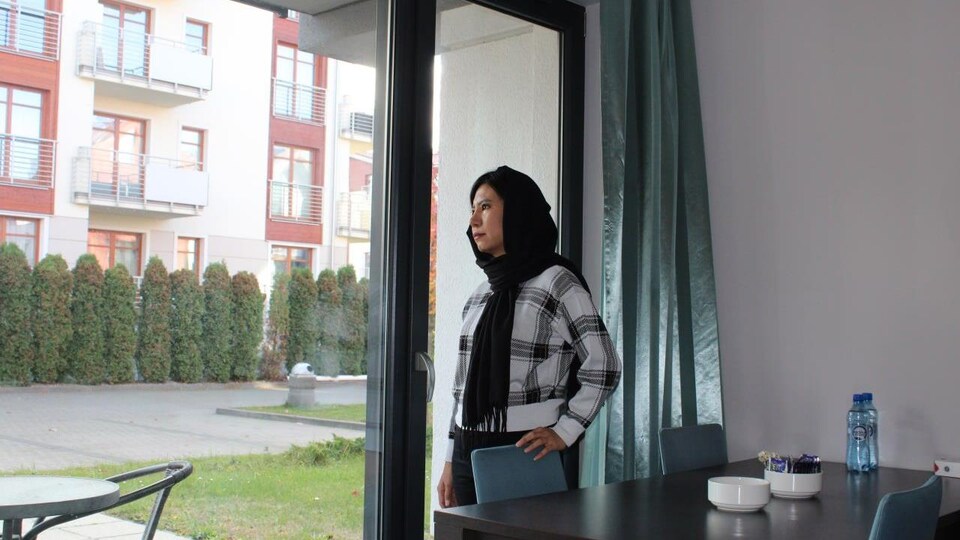 La femme afghane dans une chambre d'hôtel, regardant vers l'extérieur.