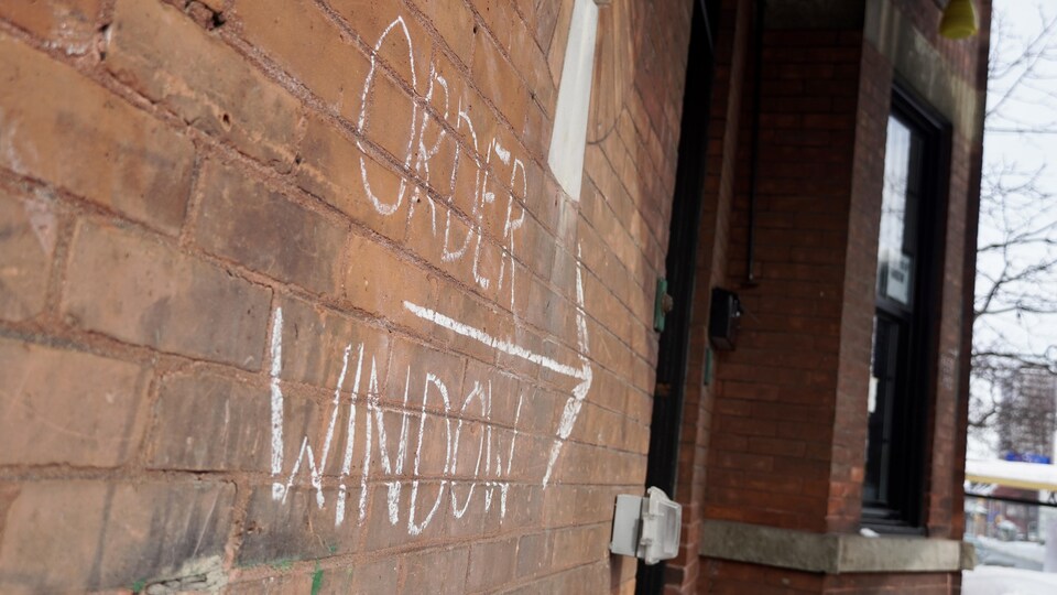Une inscription à la craie sur un mur de brique indique aux clients où est la fenêtre pour commander leur café.