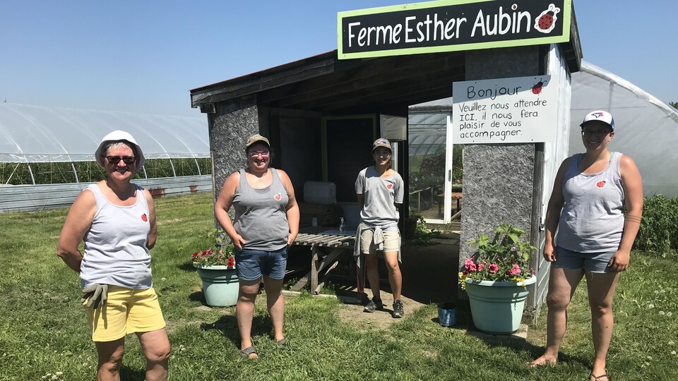Quatre femmes posent devant un cabanon avec une affiche Ferme Esther Aubin.