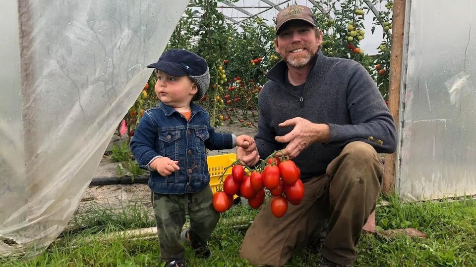 Brendan Grant tient des tomates en compagnie de son fils à l'entrée d'une serre.