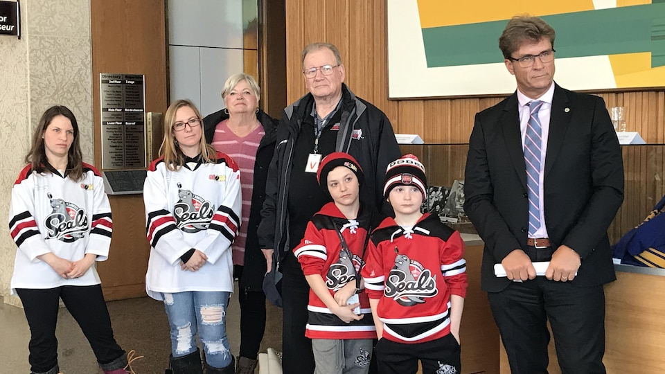 Des adultes et des enfants portant des maillots de leurs équipes de hockey, avec un homme en costume.