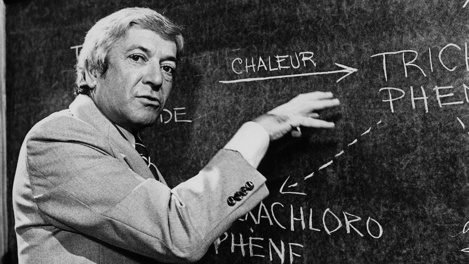 Fernand Seguin commente des concepts scientifiques inscrits sur un tableau.