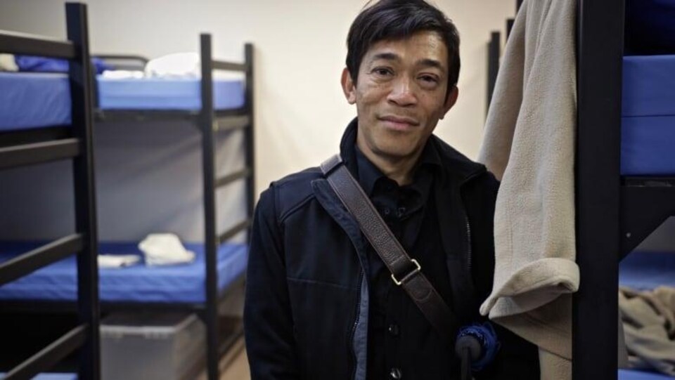 Un homme regarde devant, avec des lits superposés en arrière-plan.