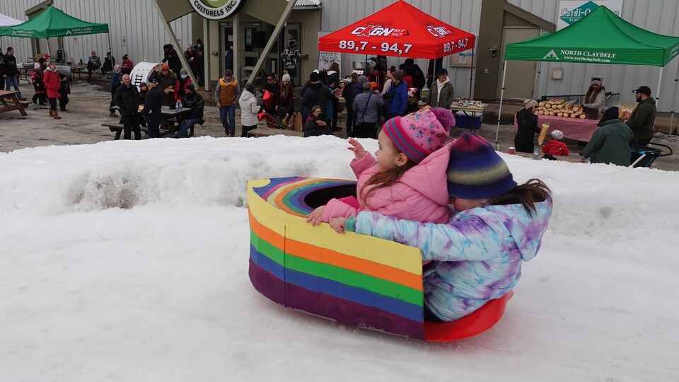 Deux enfants glissent dans une luge transformée en bateau multicolore.