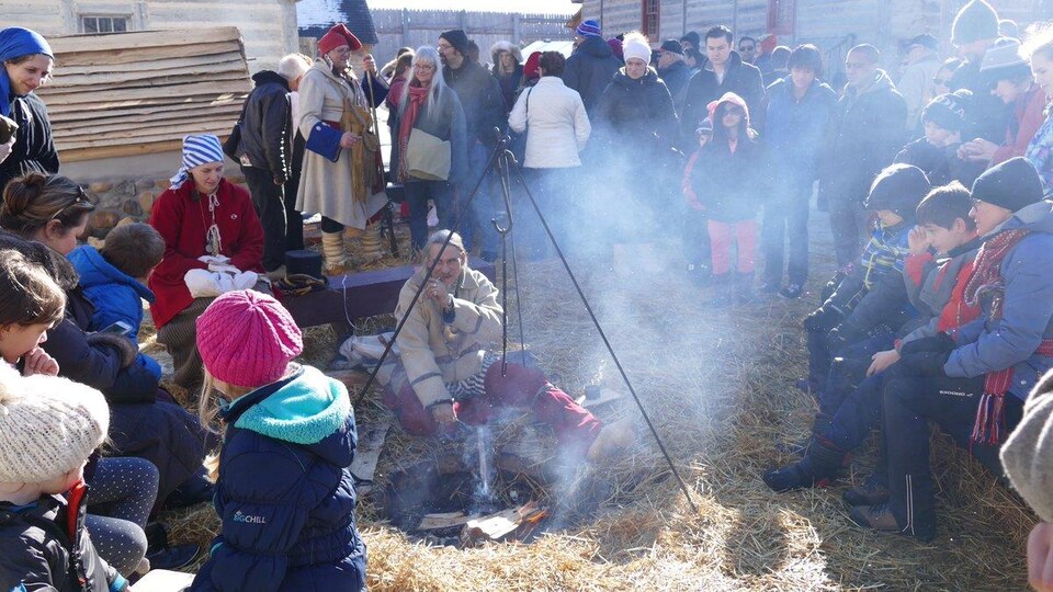 des personnes qui sont assises ou debout autour d'un feu de camp, dans l'enceinte exrtérieure du fort Gibraltar.