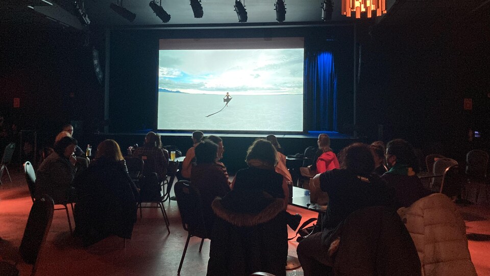 Des gens sont assis dans une salle où un film est projeté sur un écran.