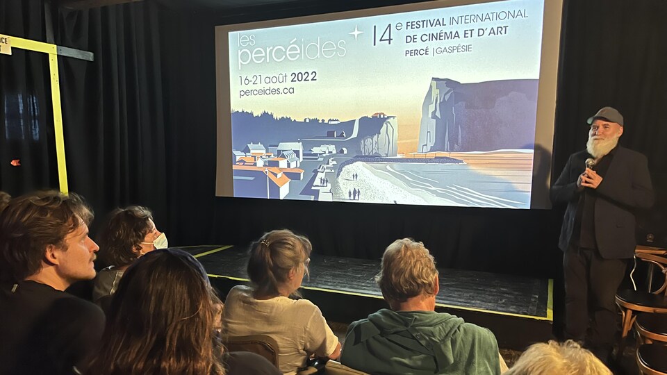 François Cormier devant une foule assise au cinéma et avec le logo du Festival affiché sur grand écran.