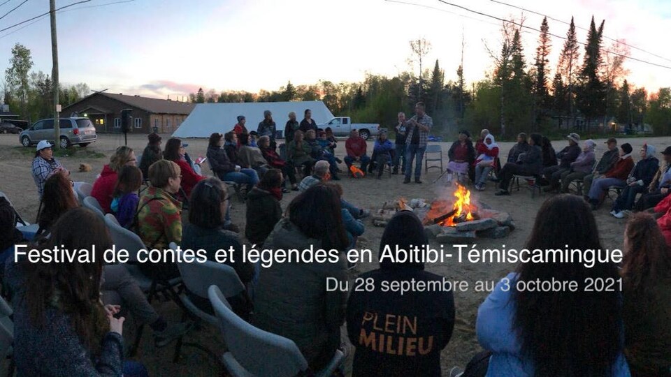 Un public assis en cercle autour d'un feu de camp à l'extérieur.