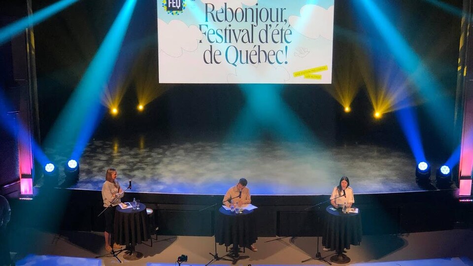 Les membres de la direction du Festival d'été de Québec devant une scène dans une salle de spectacle intérieure.