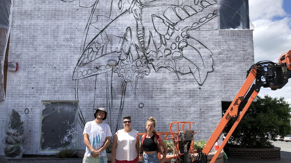 Trois personnes devant une immense murale de papillon. 