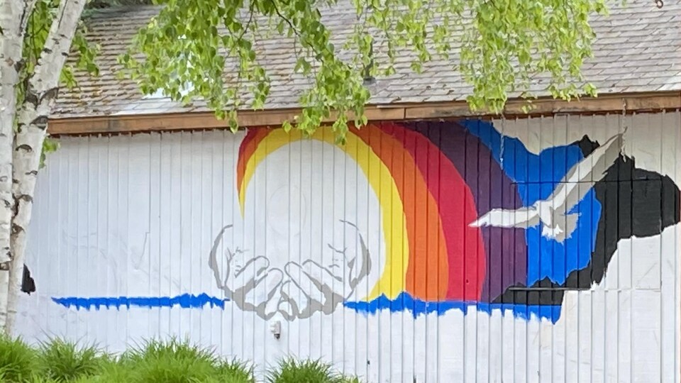Une murale d’une vague de couleurs, de mains et d’un oiseau sur un mur. 