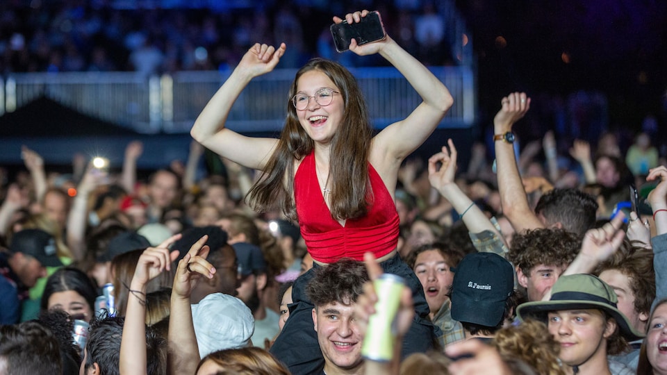 Une jeune fille, assise sur les épaules d'un spectateur, lève les bras dans les airs.