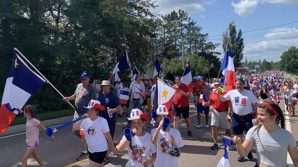 Des gens marchent dans la rue avec des drapeaux de l'Acadie