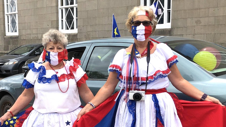 Deux femmes costumées portent des masques non médicaux aux couleurs du drapeau de l'Acadie.