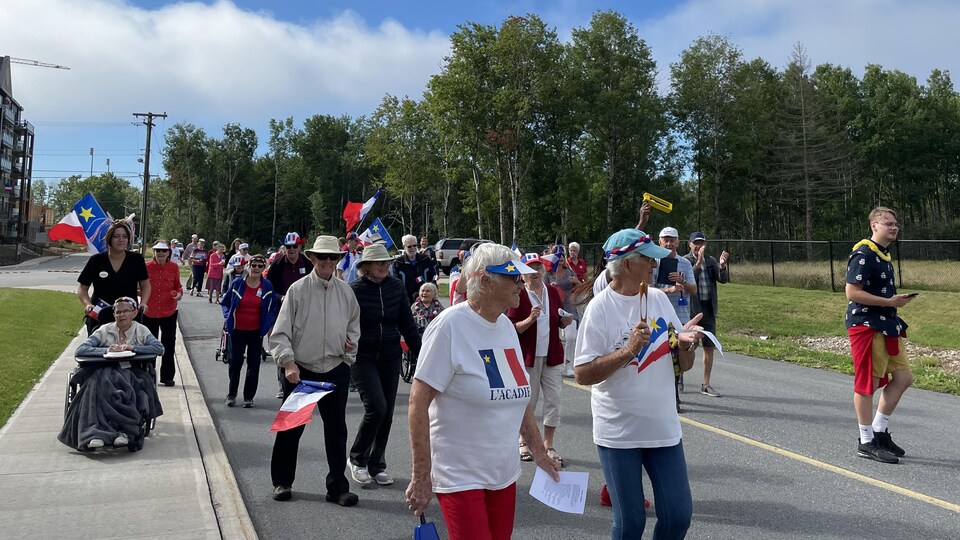 Des personnes âgées défilent dans une rue avec des drapeaux de l'Acadie.