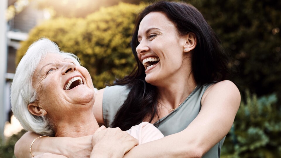 Une mère et sa fille adulte s'enlacent et rient.
