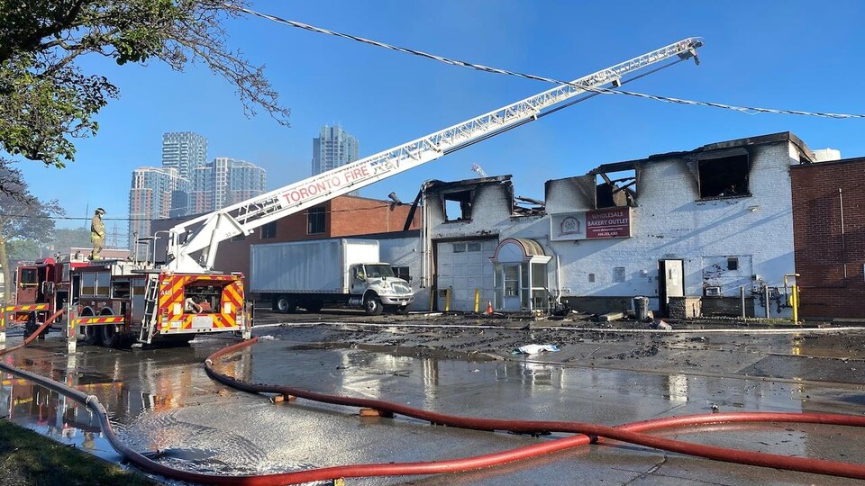 Un camion de pompier devant la boulangerie au toit effondré et aux murs noircis par le feu.