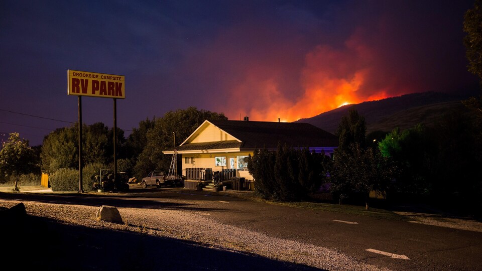 Un parc de maisons mobiles avec un feu de forêt qui brûle en arrière.