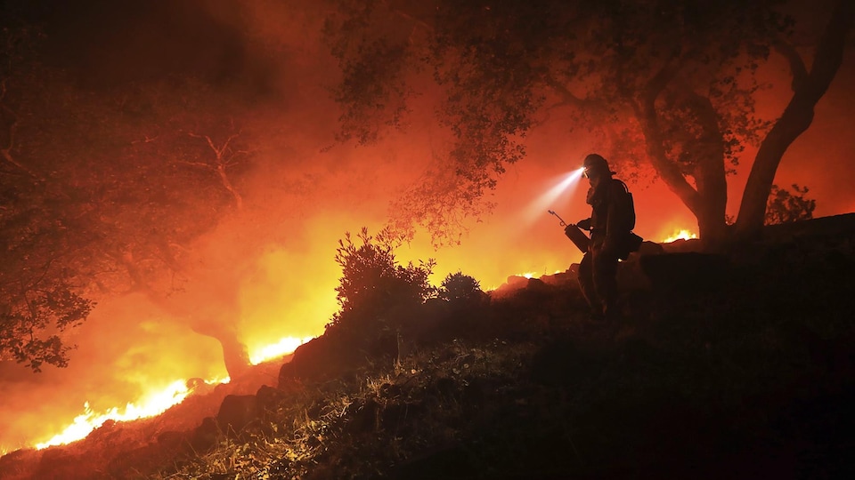 Un pompier équipé d'une lampe frontale dans une forêt en flammes