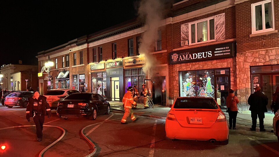 Des pompiers interviennent et de la fumée sort d'une porte le soir.
