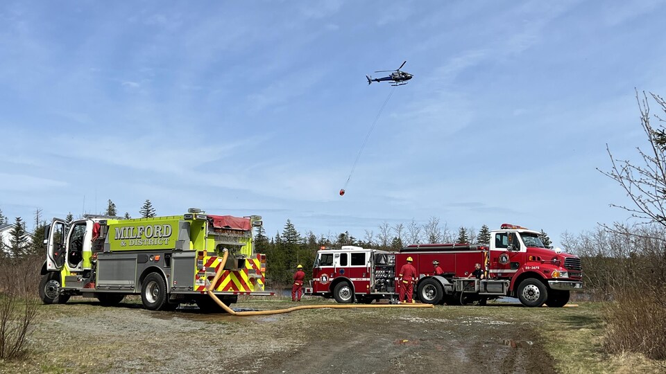 Un hélicoptère survole deux camions de pompiers.