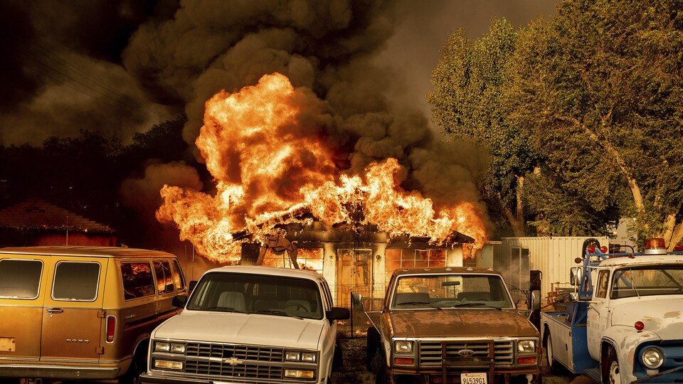 Une maison en feu derrière de vieux camions