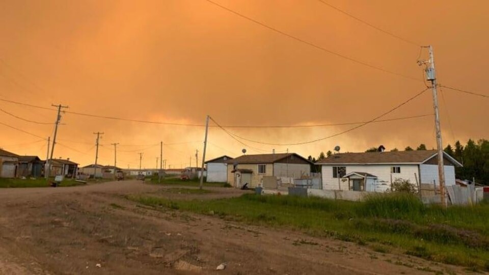 Un ciel orangé et de la fumée qui recouvrent des maisons près de Pukatawagan, au nord-ouest du Manitoba. 