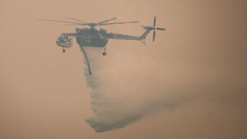 Un hélicoptère dans les airs. Il est difficile de le voir en raison de l'épaisse fumée dans le ciel.